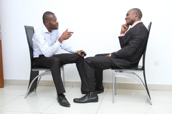 Two Black men seated and talking. Office dressed.