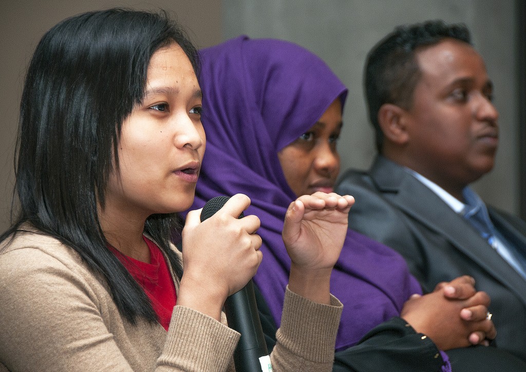 Mujer asiática, mujer moslem y hombre negro sentados en fila tomados de un lado