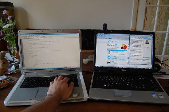 Two computers side by side, one with work on the screen, and the other with social networking