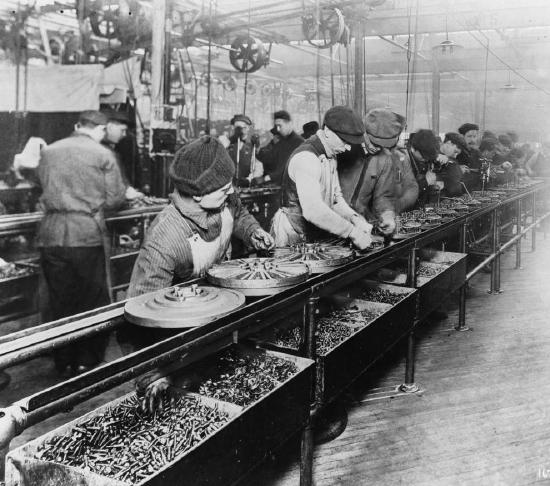An old photograph of people building hubcaps on an assembly line.