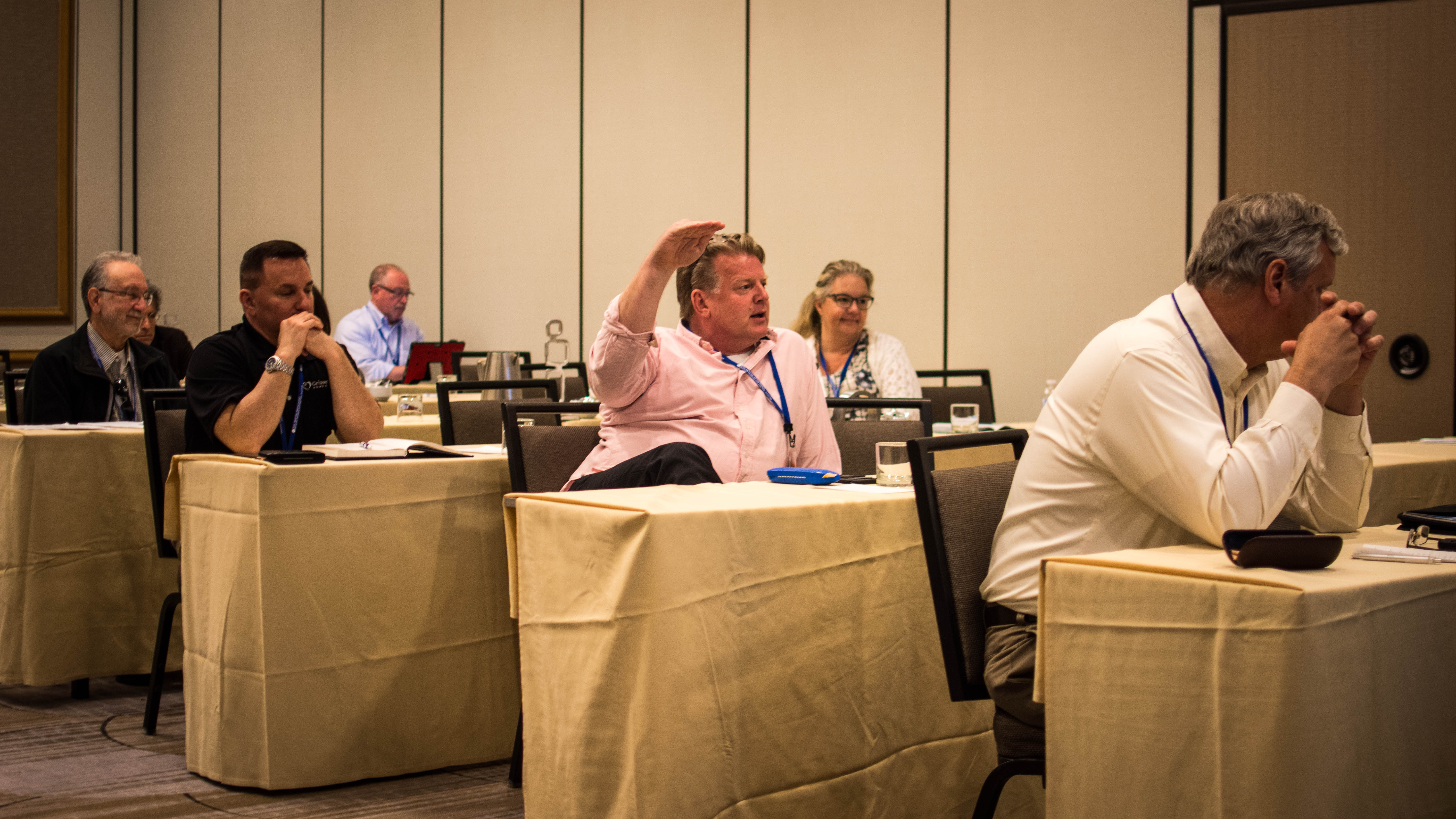 Una foto muestra a Brian Schnell levantando la mano con vehemencia mientras habla con otros abogados franquiciados durante una reunión.