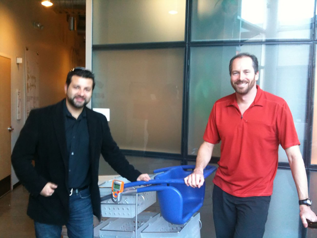 تُظهر الصورة اثنين من ممثلي IDEO الذكور وهم يقفون أمام الكاميرا مع نموذج عربة التسوق الجديدة التي قدمتها IDEO.