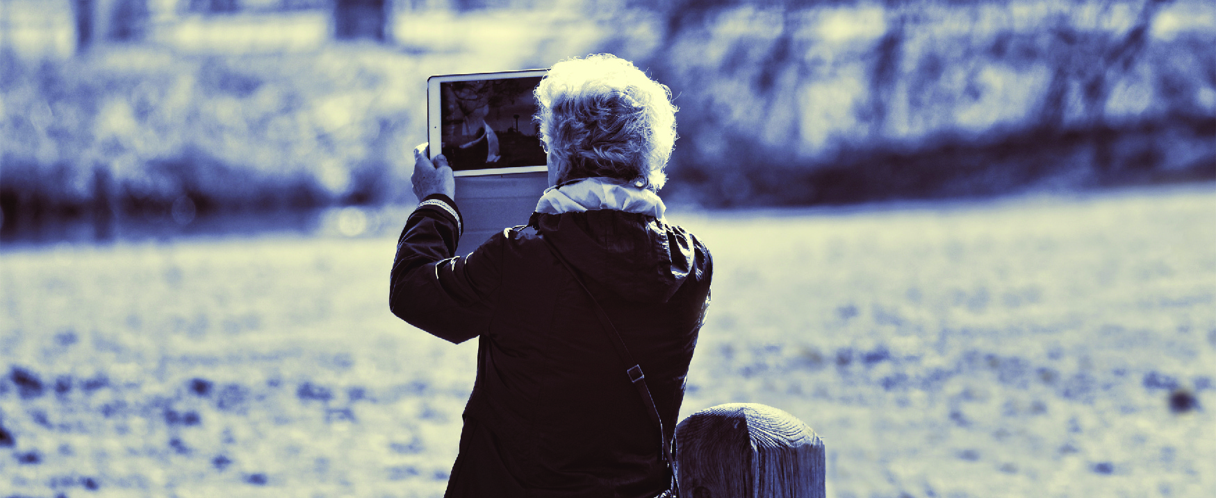 Picture of a person in a field by a stream holding up a computer tablet.