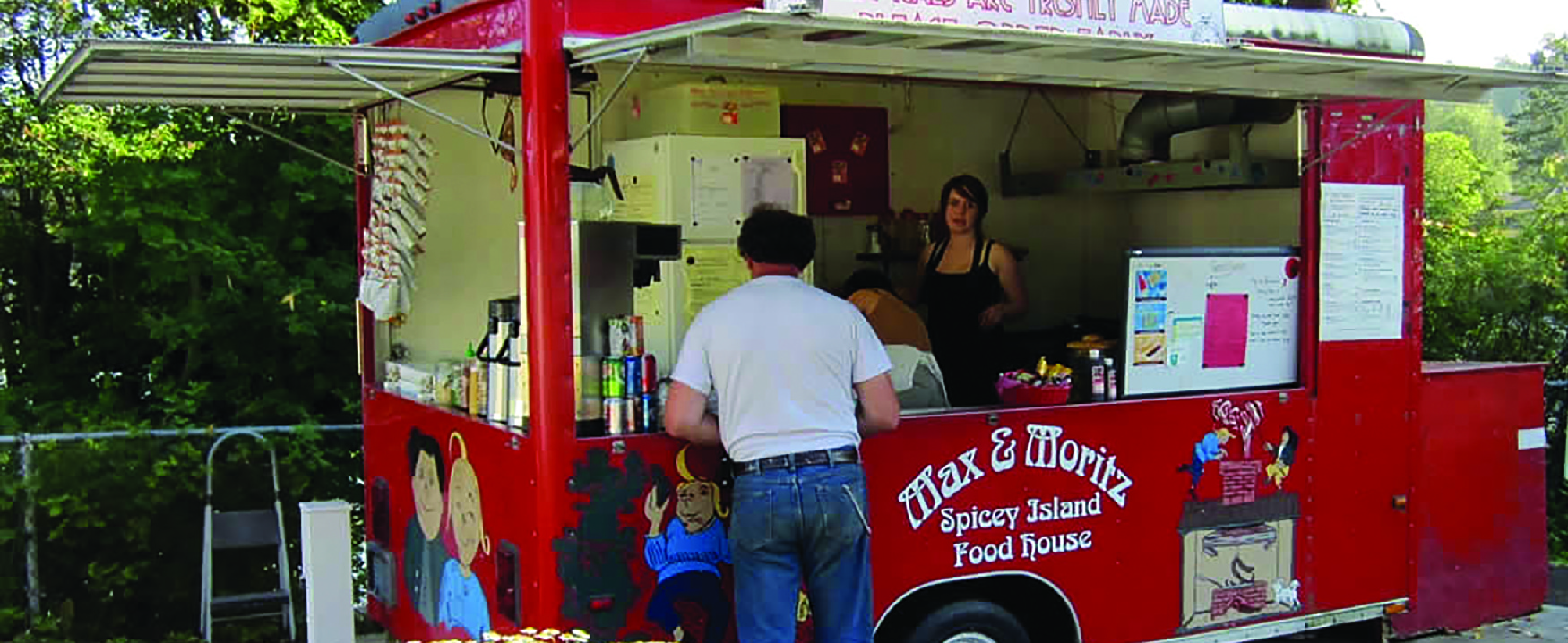 Imagen de dos personas en un camión de comida al servicio de un cliente.