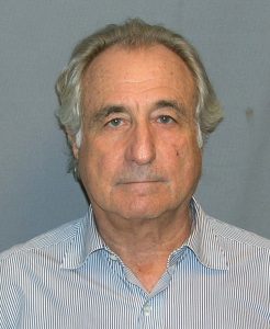 A photograph of Bernie Madoff standing in front of a blue background.