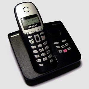 A photograph of a cordless landline phone sitting on the left side of its dock, on a white background. The phone brand is Siemens. The phone dial buttons are on the phone apparatus, with additional buttons on the dock to the right.