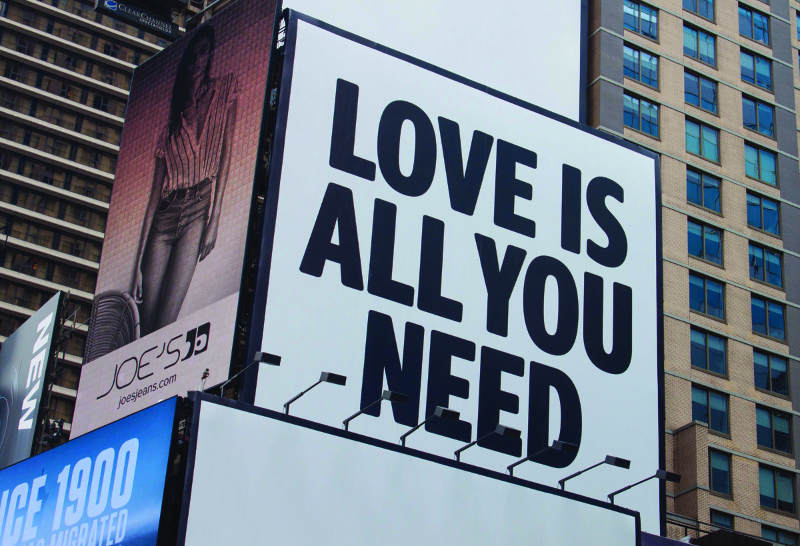 Cette image montre un panneau d'affichage sur le côté d'un bâtiment qui dit que l'amour est tout ce dont vous avez besoin.