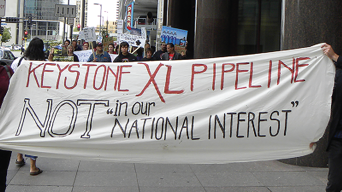 Uma faixa segurada por pessoas que diz “O oleoduto Keystone XL não é do nosso “interesse nacional”.”