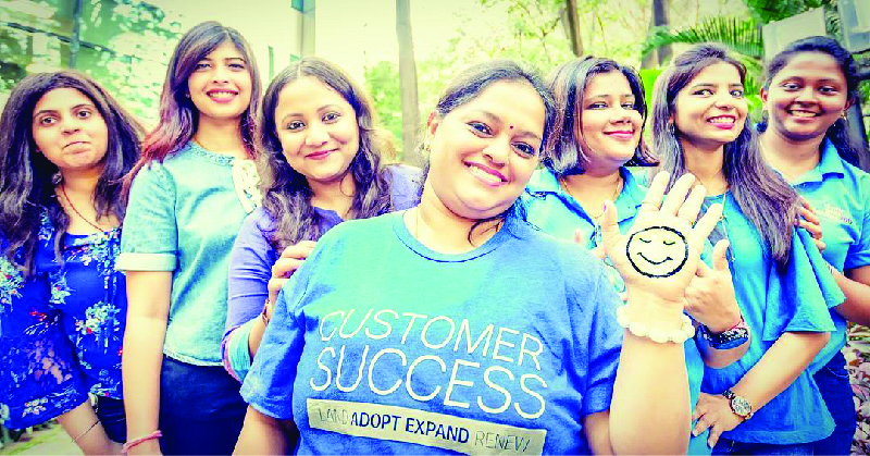 A imagem mostra sete mulheres sorrindo. A que está no centro está vestindo uma camisa que diz “Sucesso do cliente”.