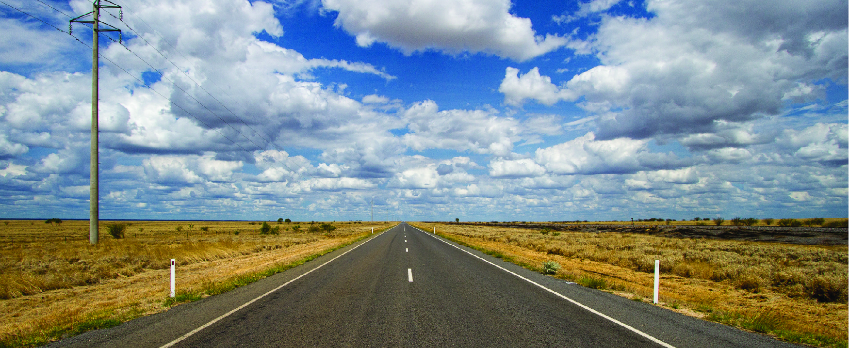 这张照片往下看一条开阔道路的中间，天空中有云彩，道路两边都有开阔的景观。