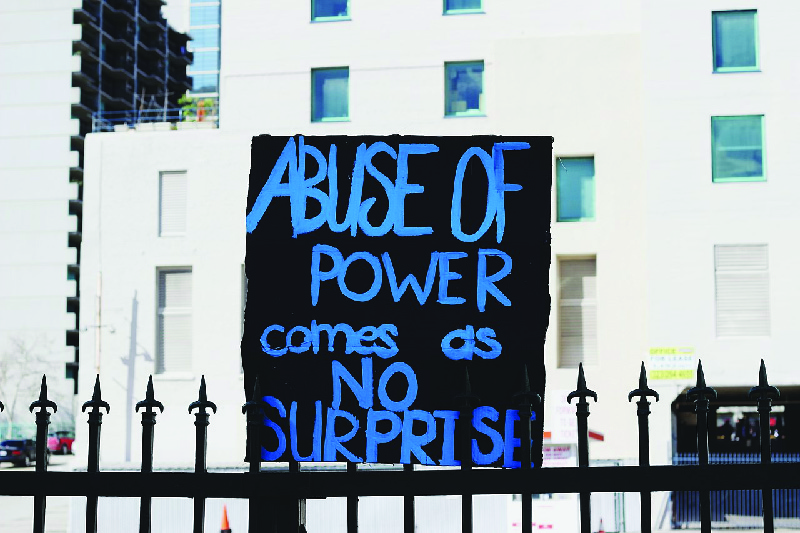 Cette image montre une pancarte peinte à la main sur laquelle est écrit « L'abus de pouvoir n'est pas une surprise ».