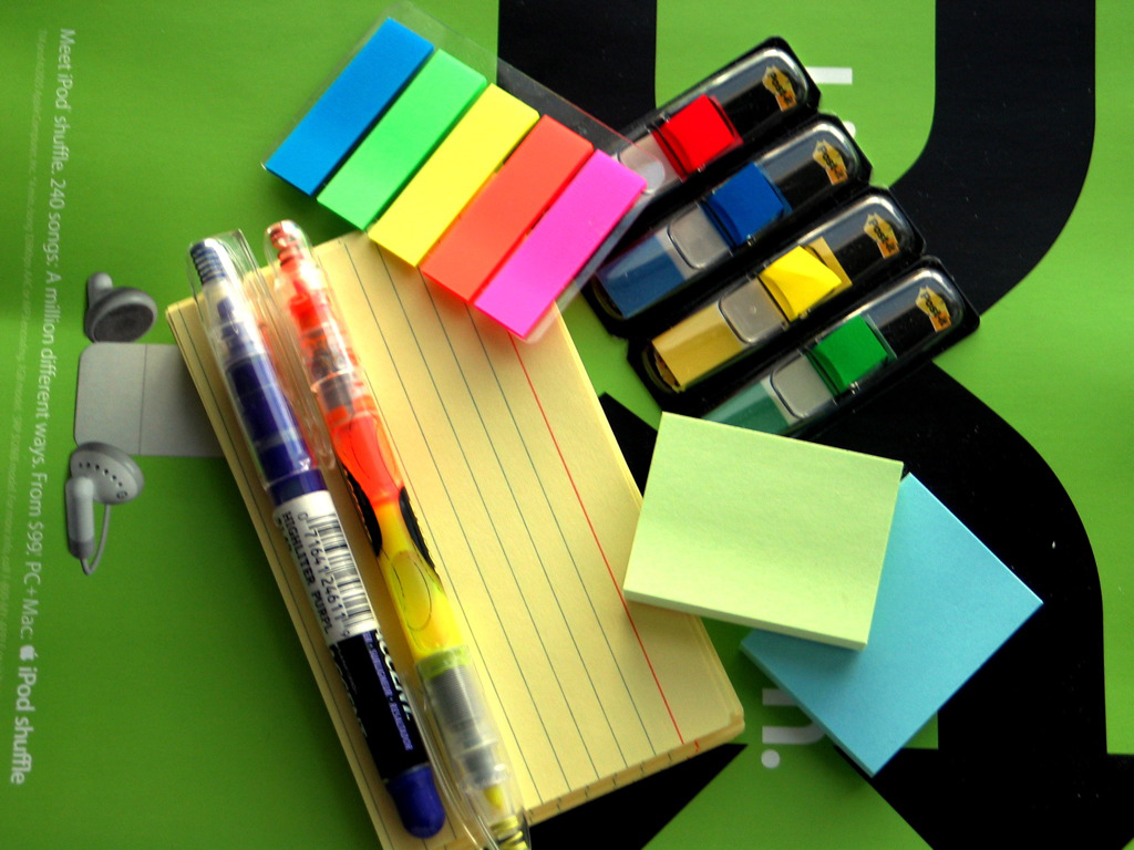 A photo shot directly from the above shows a set of stationery items including, papers, highlighters, pens, and sticky labels.