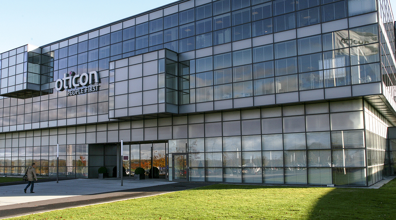 A photo shows the front view of the headquarters of Oticon, featuring modern architectural features.