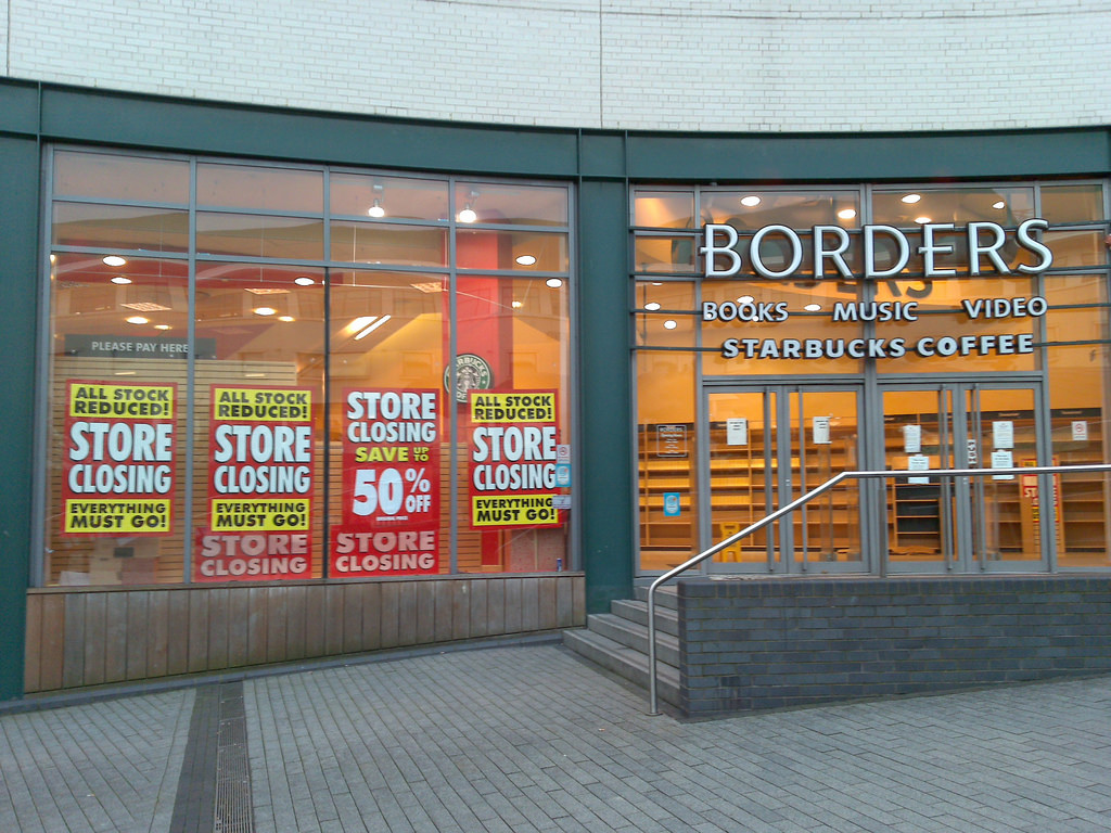 Front of a Borders store with signs in the front windows saying "Store closing! All stock reduced! Everything must go!" Other signs advertise up to 50 percent off sales.
