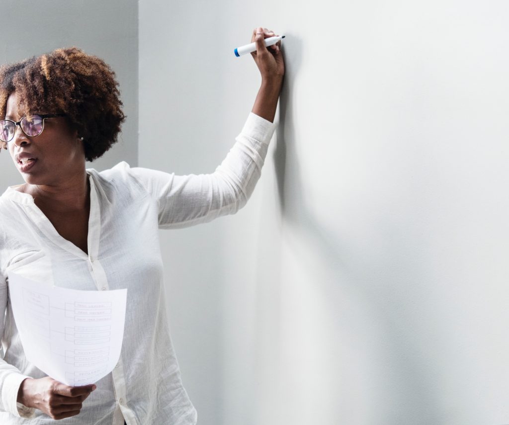 a woman standing in front of a white board ready to write with a marker