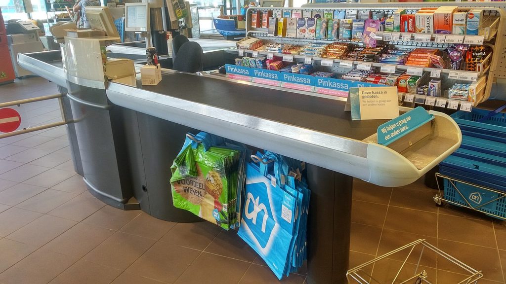 a check out counter in a grocery store with many shelves with items to sell while customers are in line.