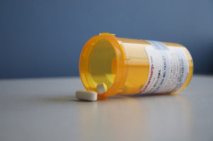 Pill bottle lying on its side with tablets spilling on the table