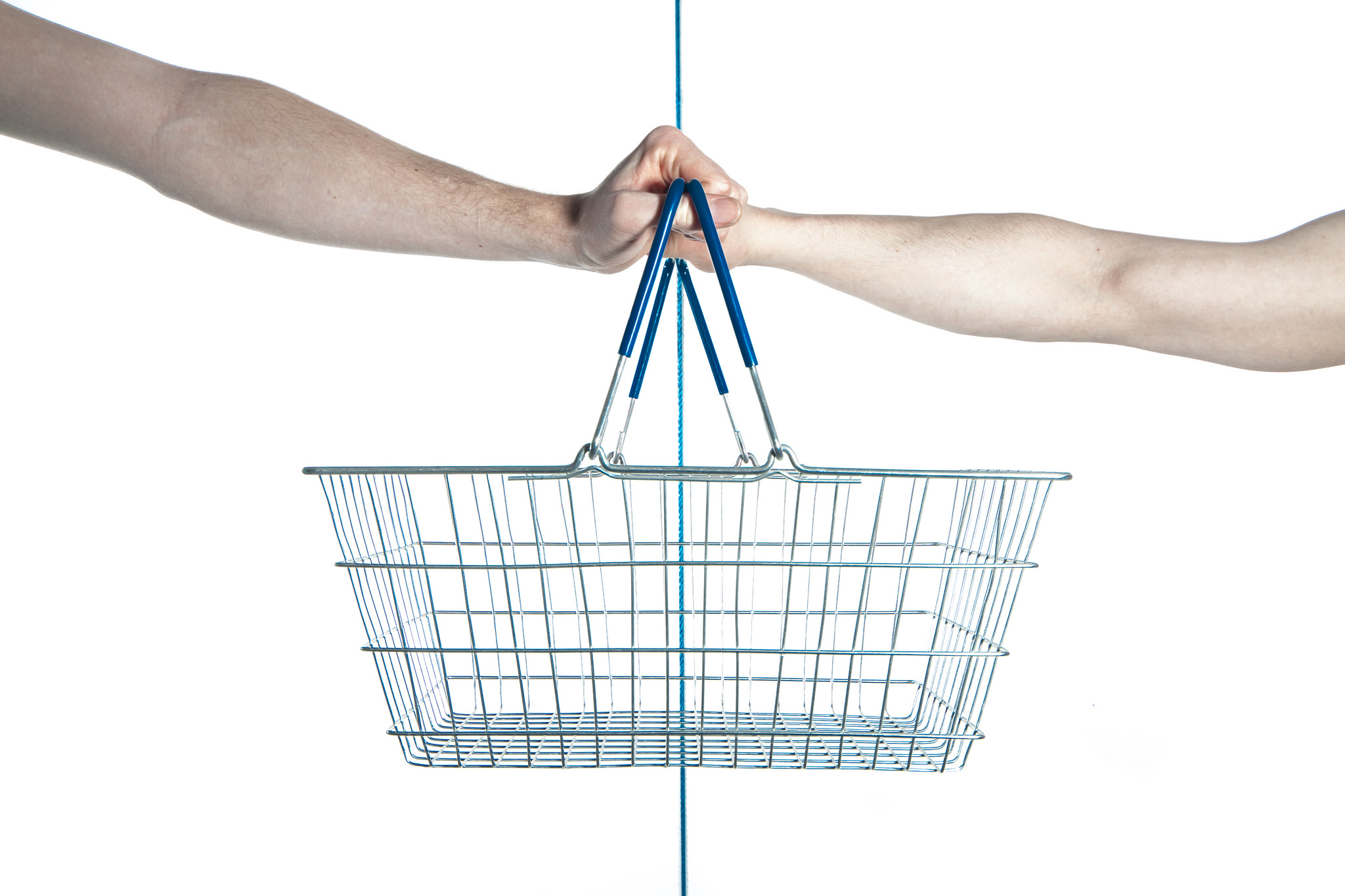 An empty wire shopping basket held by two different hands on opposite sides.