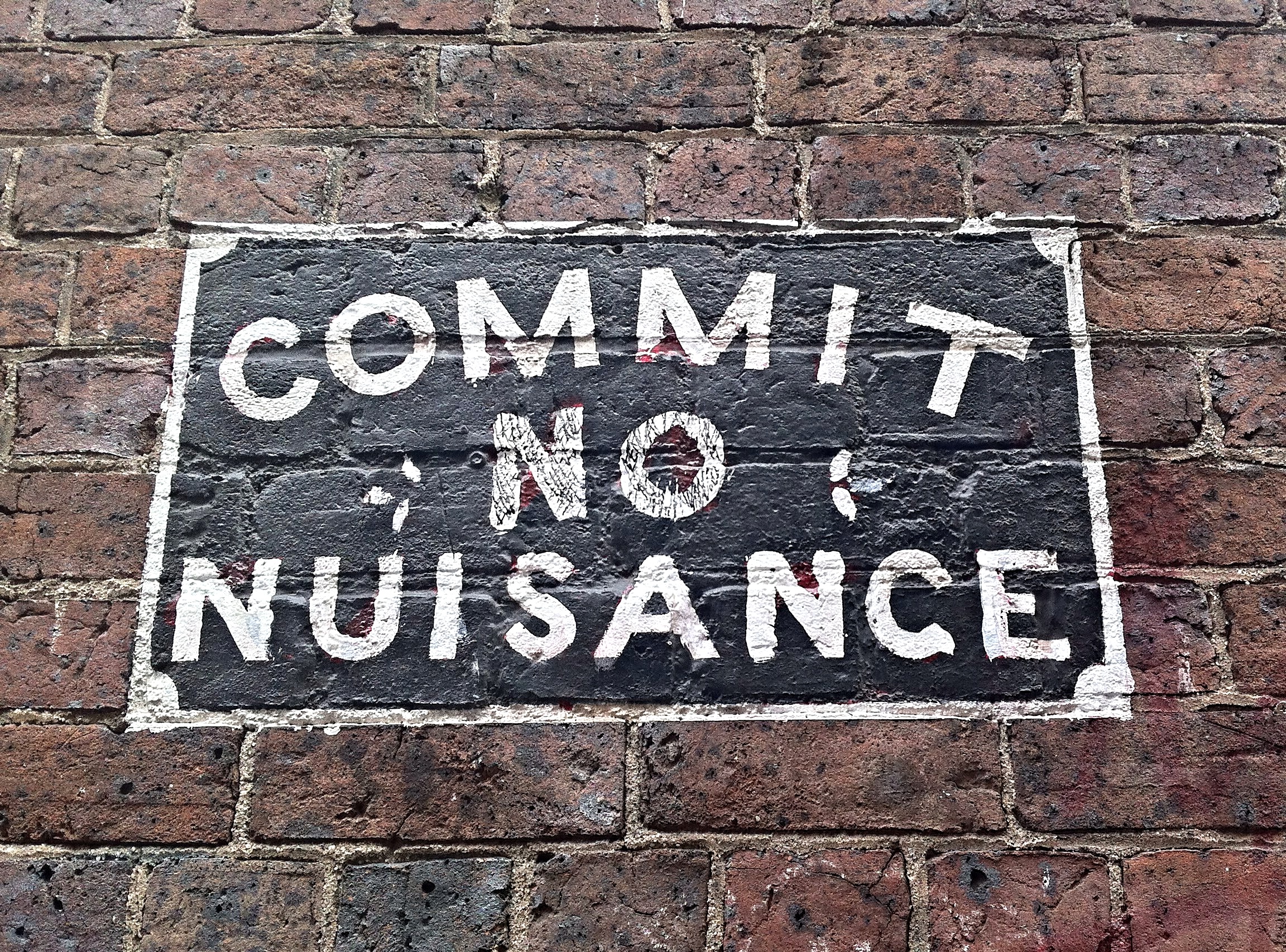 Sign on a brick wall that says "Commit No Nuisance."