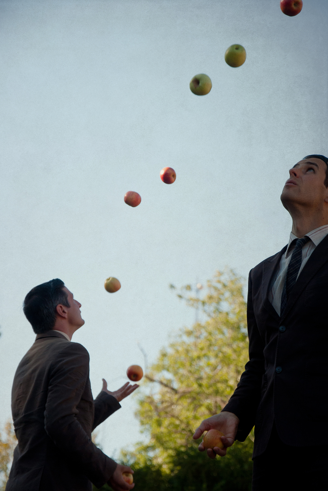 Two men wearing suites juggle apples