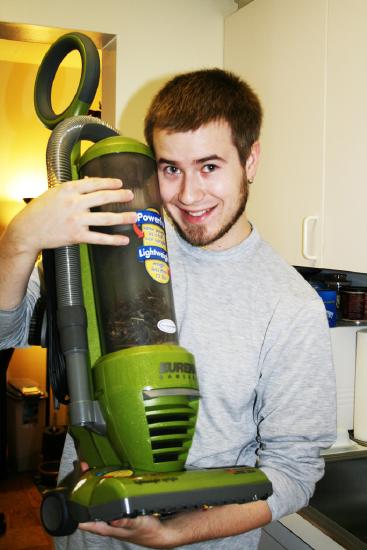 a smiling young man holding a vacuum cleaner