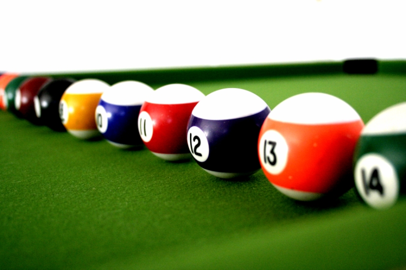 A row of striped pool balls on a green pool table with numbers facing forward (10, 11, 12, 13).
