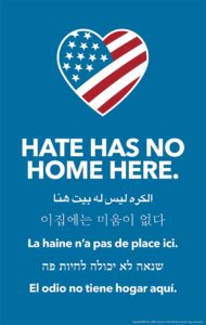 Sign that has the American flag in the shape of a heart and the text "hate has no home here" in English and five other languages.