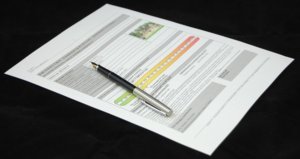 A piece of paper is displayed on a black table. The paper has ineligible text on it and a half black and half silver pen laying on top of it.