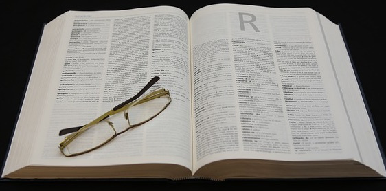 A dictionary has been opened to the page where all words that begin with R is. On the dictionary is a folded pair of reading glasses.