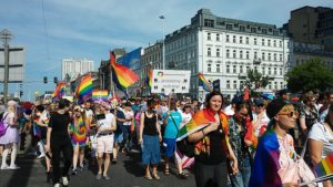 A crowd of people with large rainbow flags marching down a street in Warsaw, Poland.