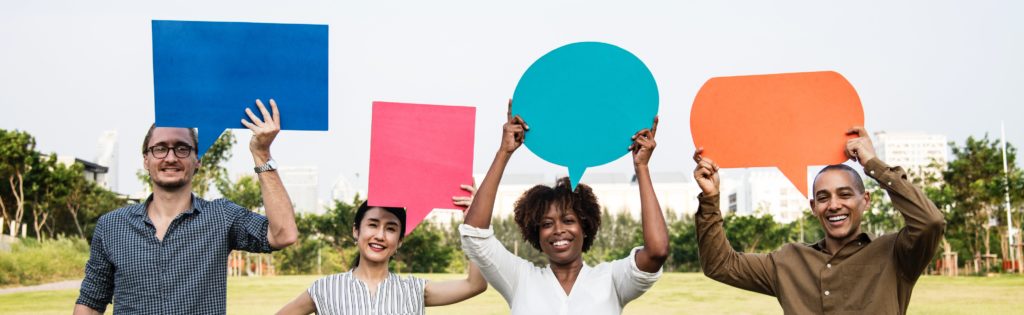Photograph of four people holding different colored blank speech bubbles above their heads.