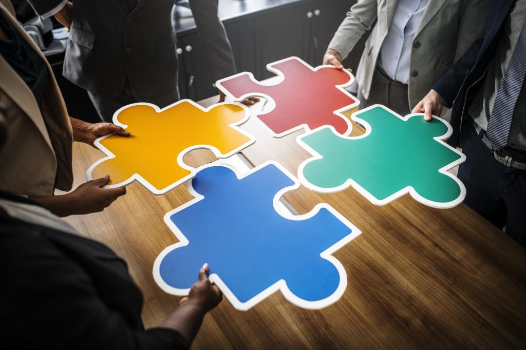 Photograph of four large puzzle pieces held by four different people.