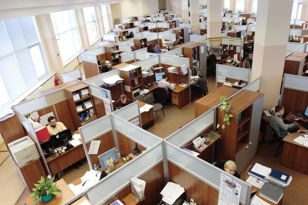 Aerial photograph of an office. The room is full of open cubicles. Most cubicles have an employee sitting at a desk.