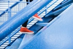 A person wearing red tennis shoes walking up a blue staircase.