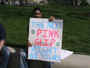 Man holding sign "the next pink slip might be yours"