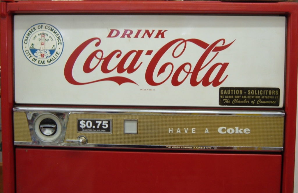 Vintage Coca-Cola vending machine with slogan 'Drink Coca-Cola' in large stylized letters and smaller slogan 'Have a Coke'. Price for one Coke is set at $0.75
