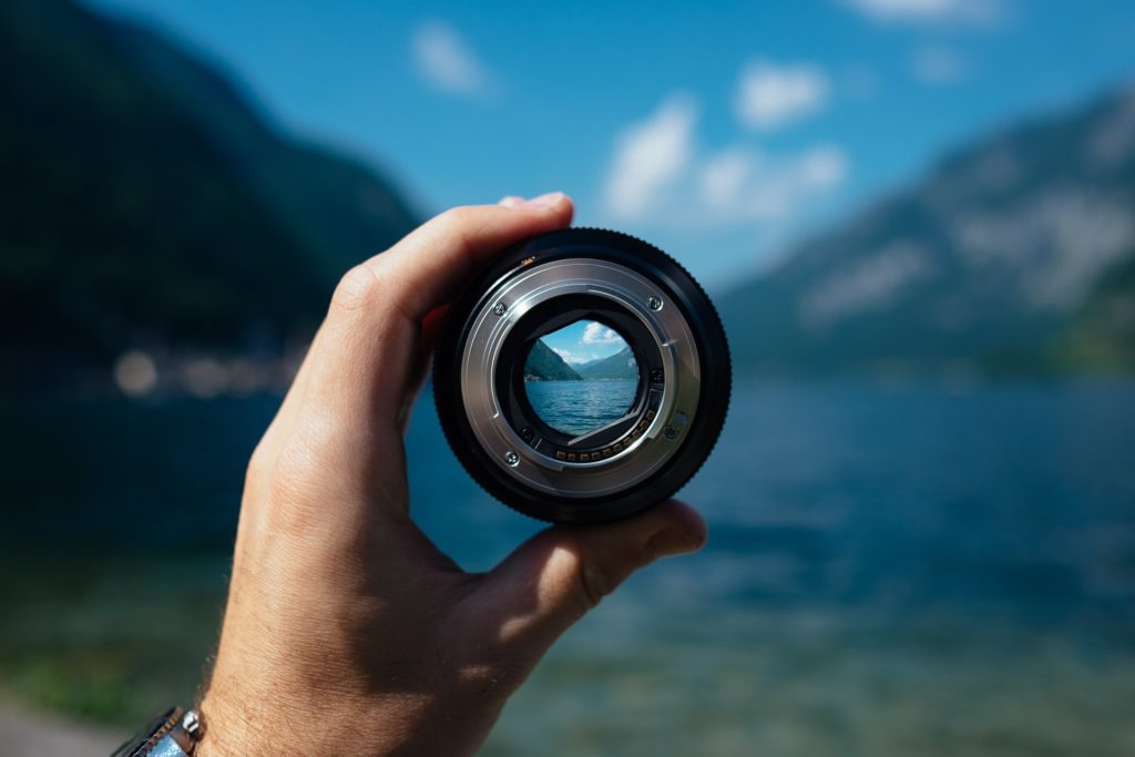 hand holding a camera lens looking at a mountain scene