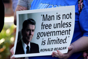 Person holding a sign with a picture of United States President Ronald Reagan. Sign says "Man is not free unless government is limited. -Ronald Reagan"