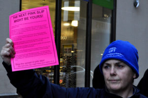 Woman holds up a pink paper. The paper says "the next pink slip might be yours!".