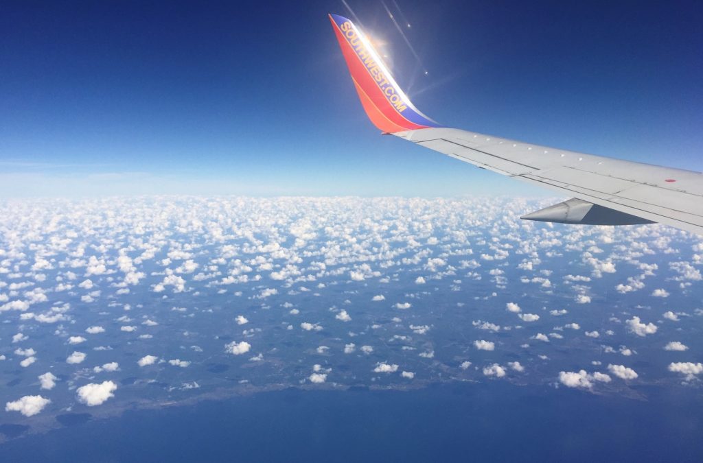 Southwest Airline plane wing with the sea, land, and clouds below.