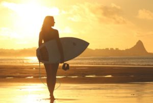 A woman walking on the beach at sunset holding a surfboard