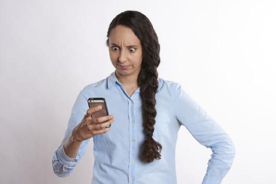 Photograph of a woman looking at a mobile phone. She looks upset and a little surprised.
