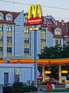 A McDonald’s sign with a gas station and residential building in the background.