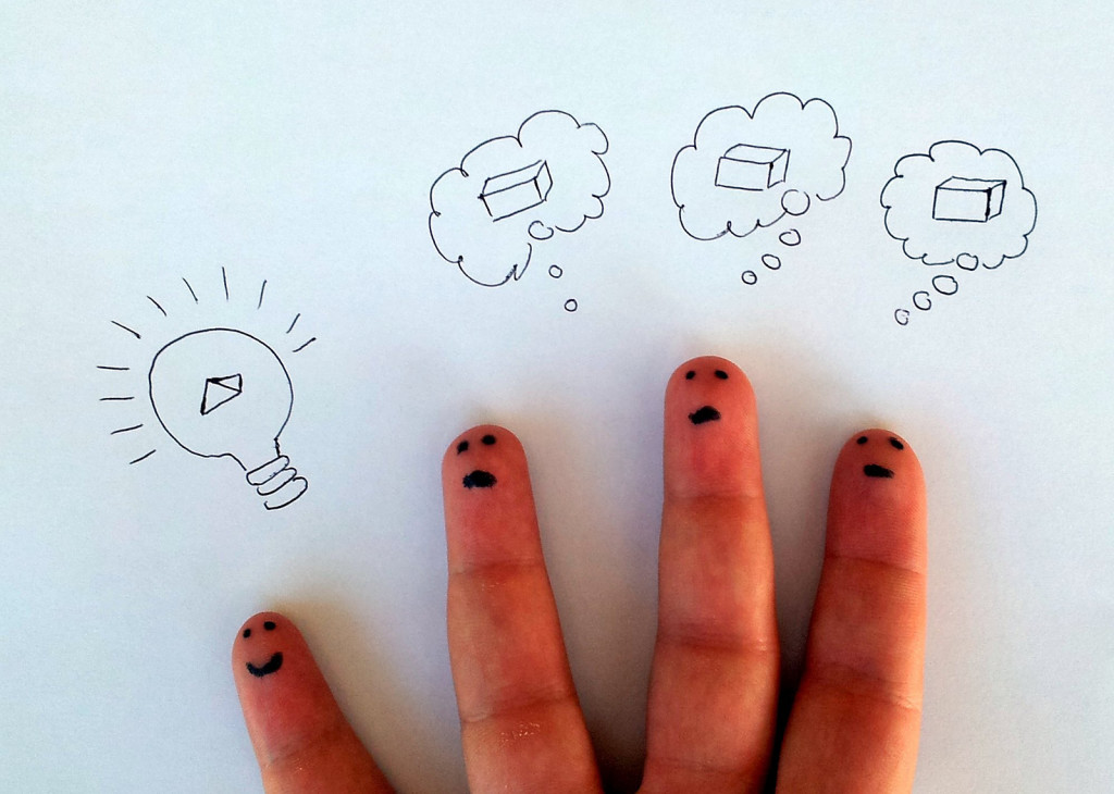 Photo of four fingers, each with a face drawn on the fingertip. Above the pinky is a drawing of a lightbulb with a pyramid inside. Above each of the three other fingers is a "thought bubble" with a picture of a box inside. The lightbulb finger is apparently "thinking outside the box," unlike his finger peers.