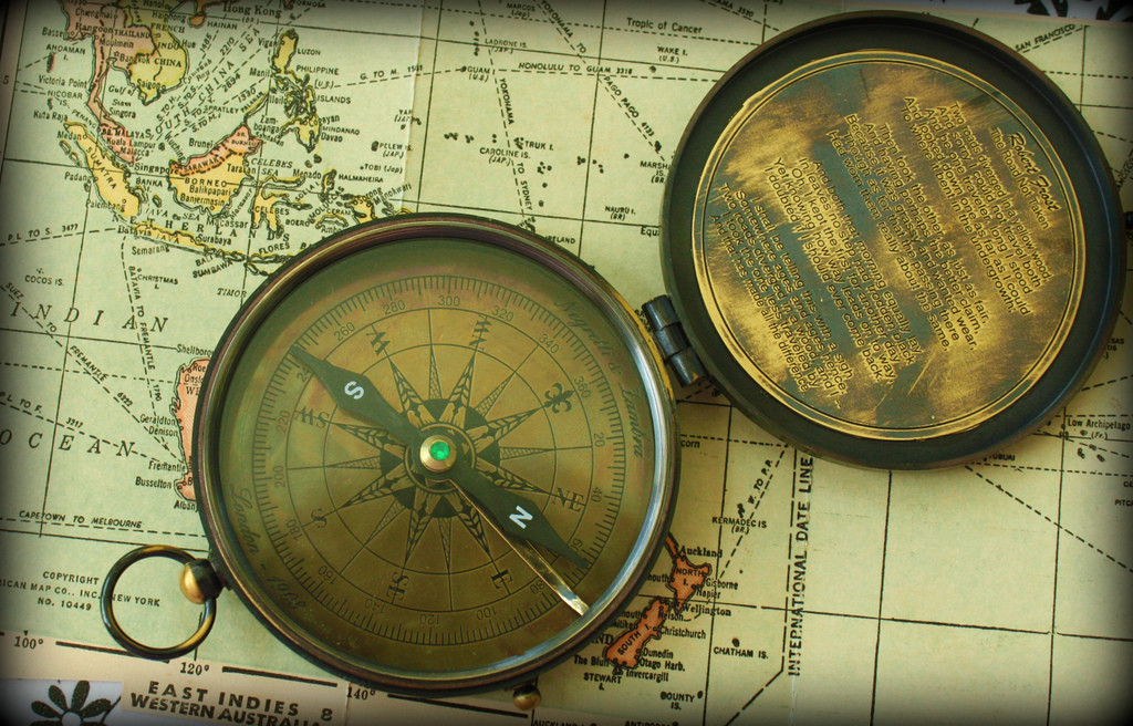A vintage brass compass lies atop a vintage map.