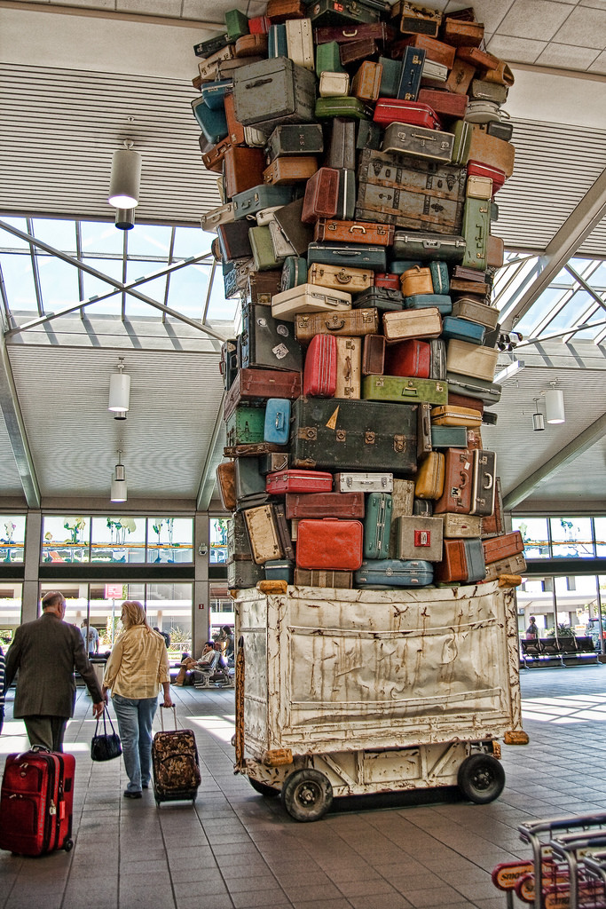 A canvas trolley is stacked so high with lost luggage that it reaches all the way to the ceiling of an airport.