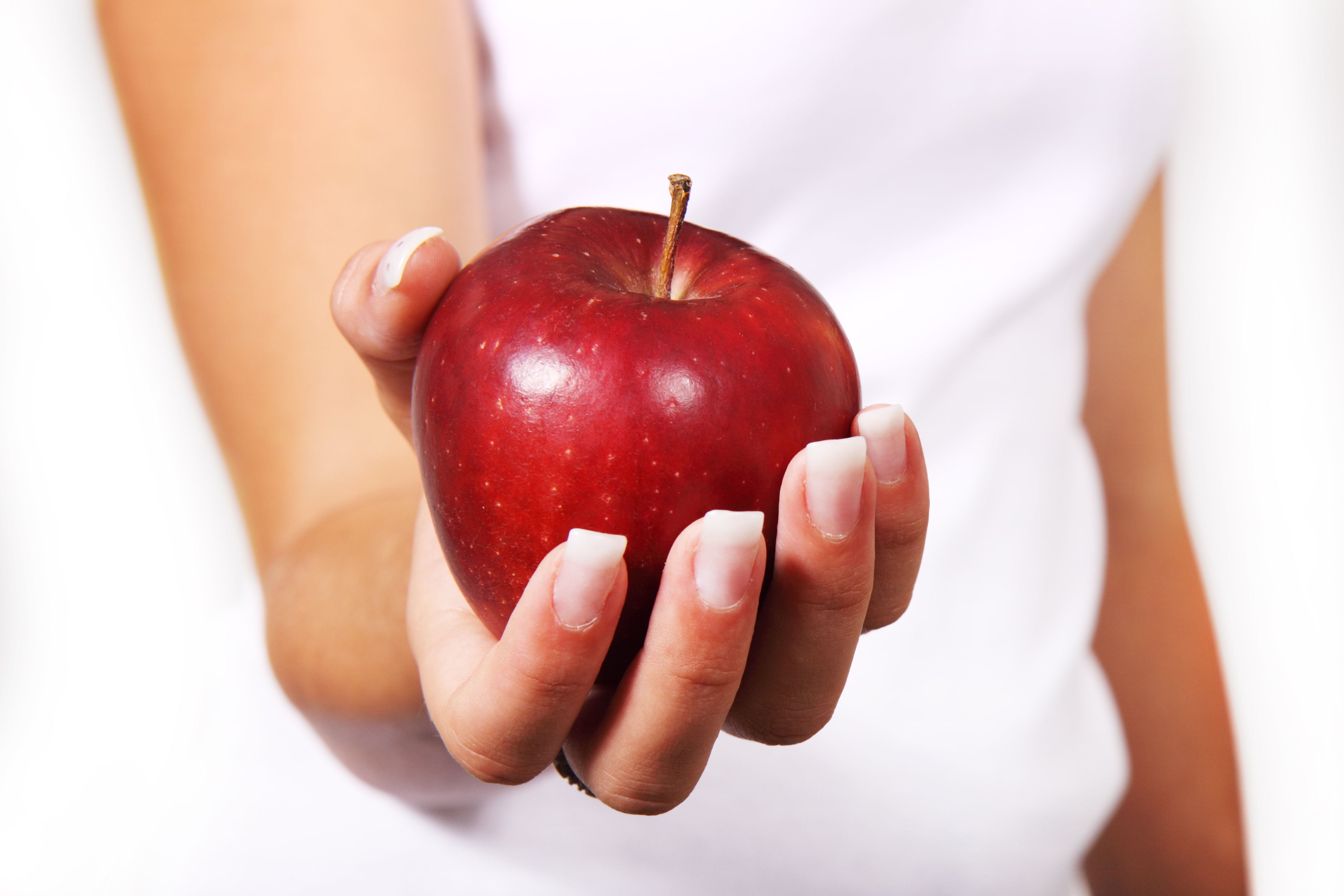 A red apple held in a woman's hand with her arm outstretched as if offering it to the viewer.