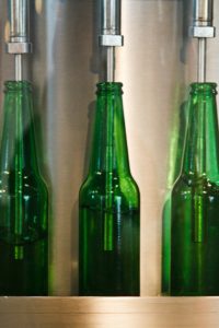 Three green twelve ounce bottles on a production line. The bottles are being filled with a liquid.
