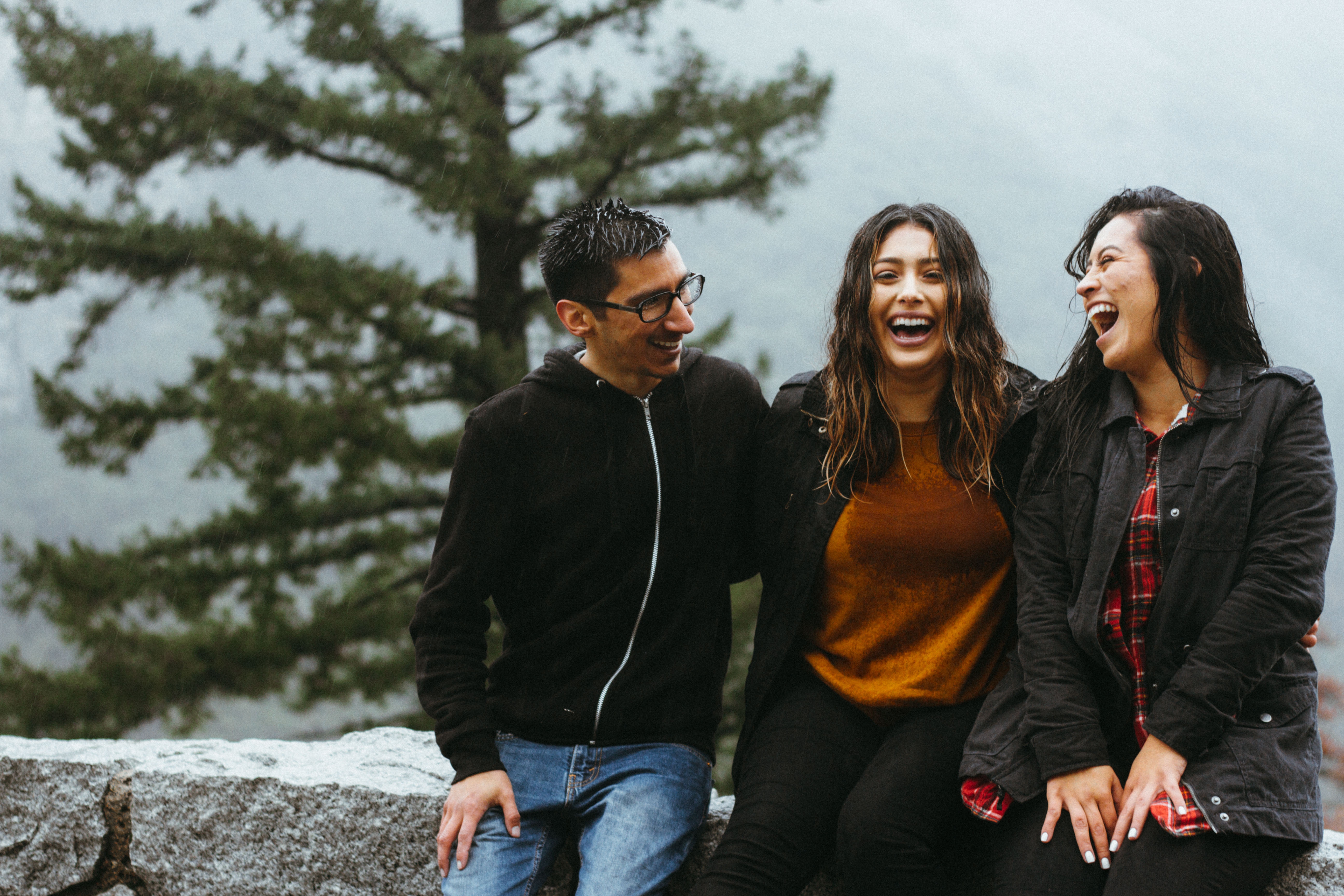 A man and two women sit on a stone wall and they are laughing.