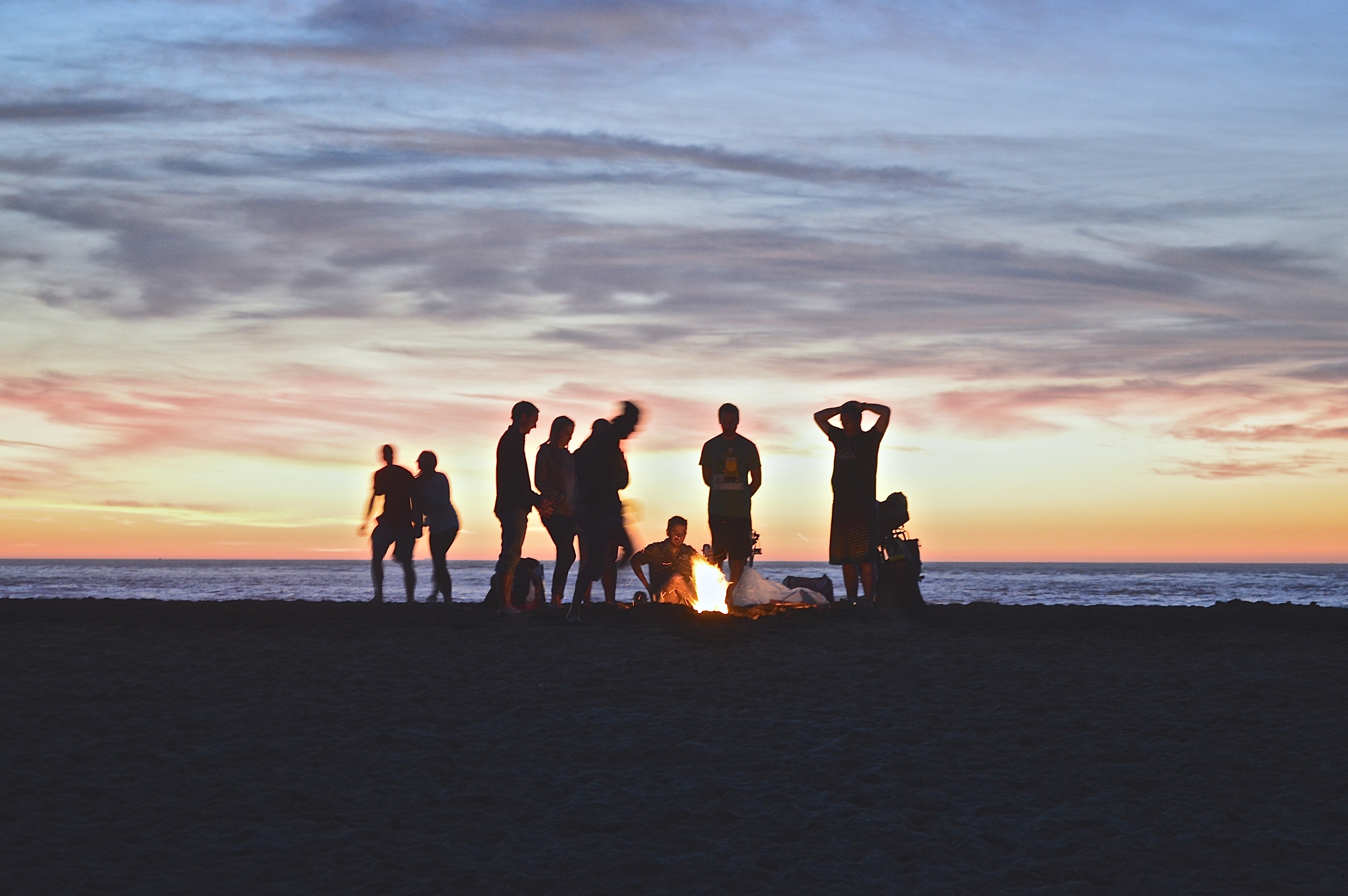several people standing around a fire on a beach.